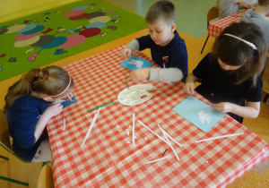 Dzieci wyklejają białym papierem szablon gołąbka.